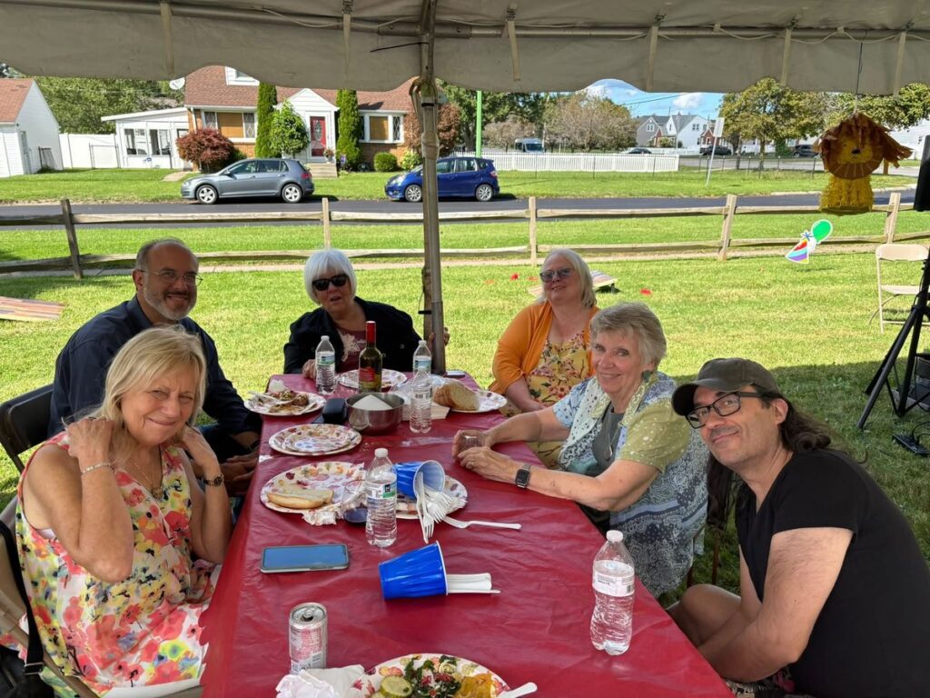 Family and friends smiling around a long red-covered Thanksgiving dinner table set up under a party tent in a backyard